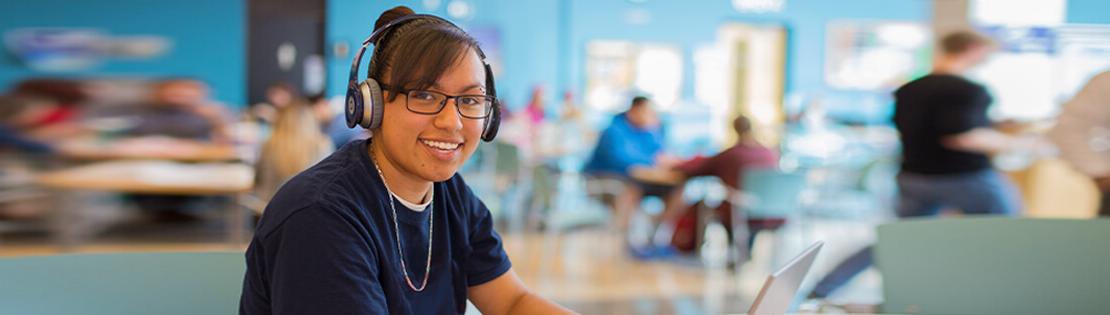 Smiling student sits and works on her computer in a student lounge